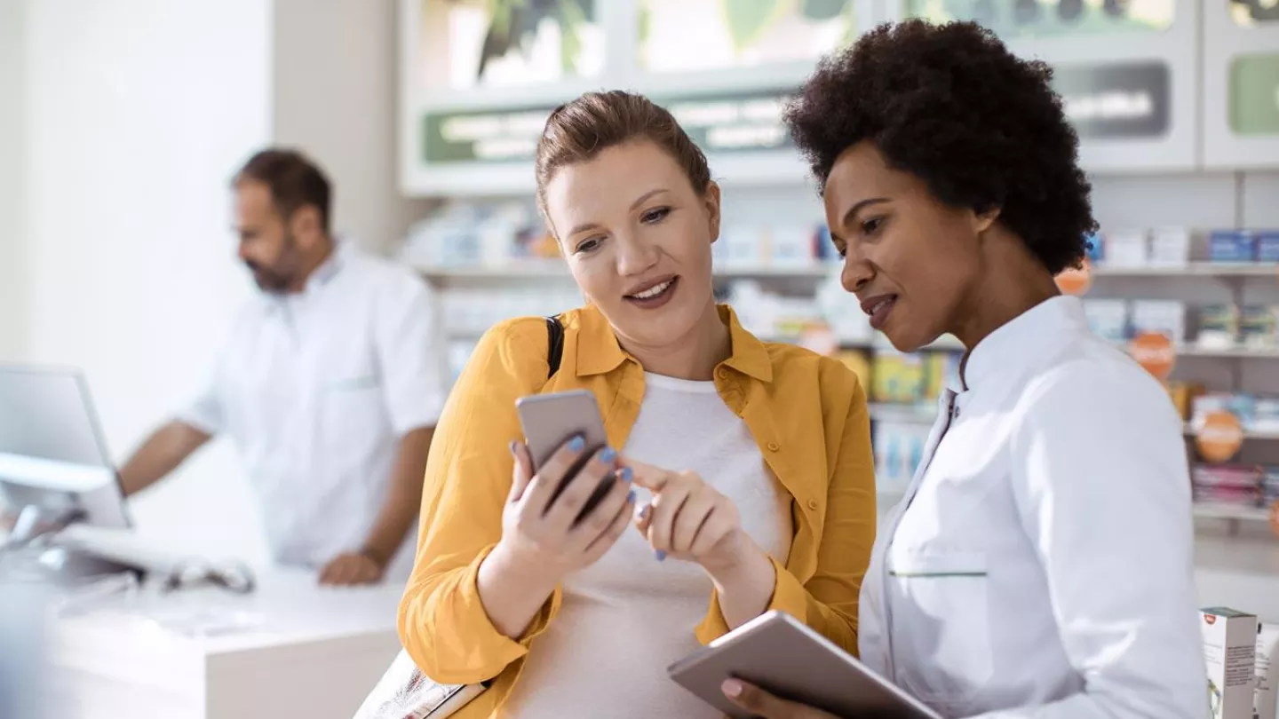A phamacist helps a woman with a purchase using a phone